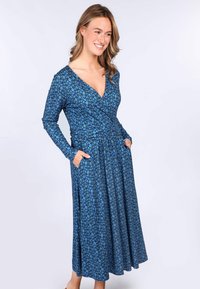 Blaues Blumenwickelkleid mit langen Ärmeln, Taschen und einem fließenden Rock. Hergestellt aus weichem Stoff mit kleinen, hellblauen Blumen auf dunklem Hintergrund.