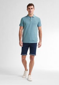 Polo de color azul claro con mangas cortas, combinado con pantalones cortos oscuros enrollados. Atuendos complementados con zapatillas beige. Textura de tela suave.