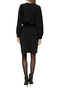 Czarna sukienka dresowa z długimi rękawami, okrągłym dekoltem i ściągniętą talią; zestawiona z czarnymi botkami na wysokim obcasie.