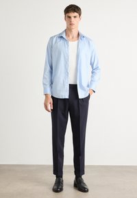 Light blue long-sleeve shirt, buttoned with a pointed collar, paired with dark navy tailored pants and black shoes. Simple, clean design.