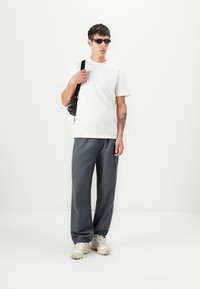 Hvit bomull t-skjorte, grå løstsittende bukser og beige sneakers. Tilbehøret inkluderer en liten svart crossover-veske. Kort hår, solbriller. 