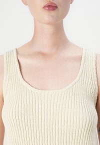Beige strikket tank topp med ribbet tekstur og bred, rund halslinning. Beltene er tykke, med synlige sømdetaljer.