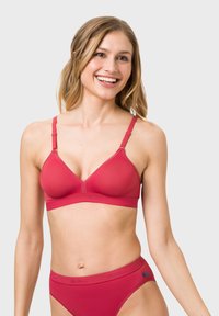Red bralette with adjustable straps, smooth texture, and a wide elastic band featuring branding. Classic triangle shape, minimalistic design.
