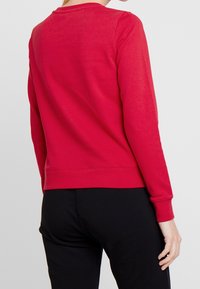 Sudadera roja hecha de un tejido suave, con mangas largas y cuello redondo. El dobladillo está a la altura de la cintura, con puños acanalados y una textura suave.
