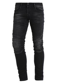 Mustat kapeat farkut haalistuneella pinnalla, joissa on vinot sauma-yksityiskohdat ja hienovarainen tekstuuri. Materiaali näyttää olevan farkkua ja se istuu tiukasti.