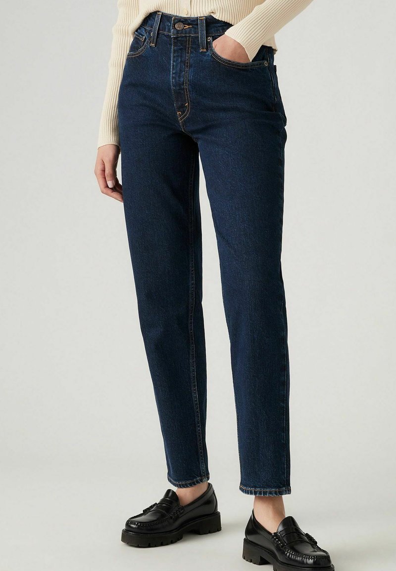 Donkerblauwe denim jeans met een hoge taille, rechte pasvorm, contrasterende stiksels en traditionele vijf-pocketontwerp. Gestyled met zwarte loafers.