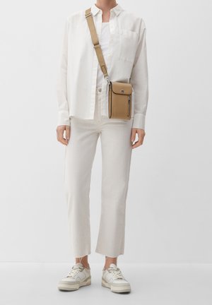 Hnědo-krémová crossbody taška s texturovaným povrchem, klopovým uzávěrem a přední kapsou na zip, doplněná o světlé džíny a bílé tričko.