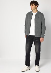 Grijze bomberjack met een subtiel zwart logo, gedragen over een wit T-shirt, gecombineerd met donkere jeans en witte sneakers. Soepele textuur, ontspannen pasvorm.