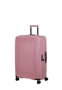 Valigia rigida di un delicato rosa, con una superficie testurizzata, manico retrattile e quattro ruote nere per la mobilità.