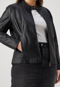 Black leather jacket with a rounded collar, zippered front, and side pockets, paired with a white top and black skirt. Smooth texture.