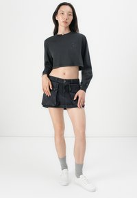Svart cropped sweatshirt med rund hals og logo, parret med et sort denim mini nederdel med forlommer. Grå sokker og hvide sneakers.