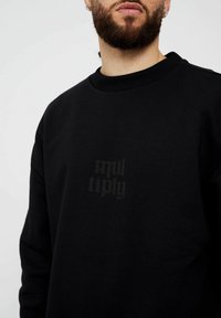 Sudadera negra hecha de tela suave, con un cuello acanalado y un logotipo oscuro impreso de manera sutil en el pecho.