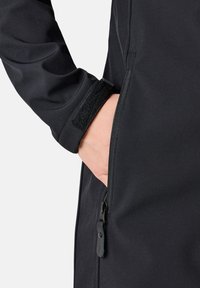 Zwarte softshell jas met een ritszak en klittenband manchet. Het materiaal is glad met een lichte glans, ontworpen voor een nauwsluitende pasvorm.