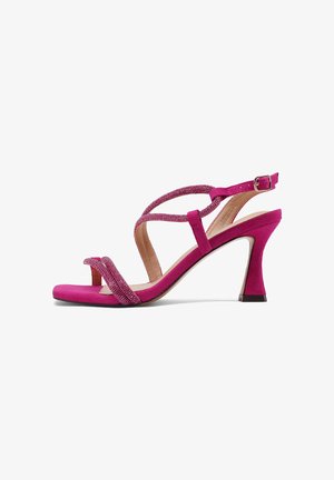 Sandalia de tacón alto magenta con tiras cruzadas adornadas con pedrería, puntera abierta, hebilla en el tobillo y tacón ligeramente acampanado sobre fondo blanco.