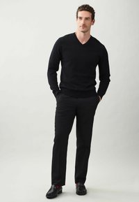 Pulover negru cu decolteu în V, pantaloni slim fit și mocasini negri cu accente roșii. Textură netedă, design simplu, fără modele vizibile.