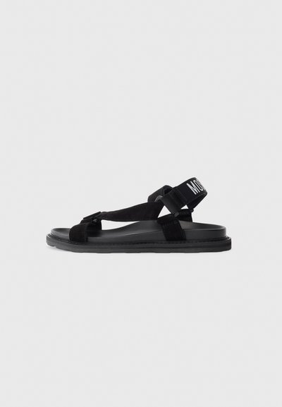 Zwarte sandalen met een platte zool, suede bandontwerp en een verstelbare enkelriem met een wit label. Lichtgewicht en minimalistische stijl.