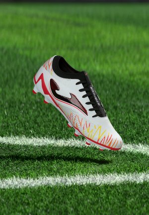 Weißer Fußballschuh mit roten und gelben Akzenten und schwarzen Schnürsenkeln, schwebt über grünem Gras in der Nähe von weißen Spielfeldlinien.