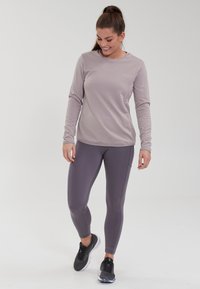 Lys grå langærmet træningstop med et struktureret design, parret med tætsiddende mørkegrå leggings. Sorte træningssko fuldender outfittet.