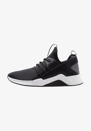 Baskets de sport noires avec semelle blanche, fermeture à lacets et col de cheville haut façon chaussette, vues de côté sur fond blanc.