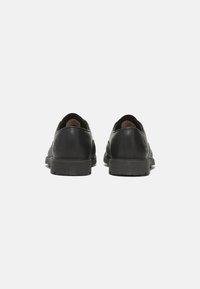 Scarpe in pelle nera con finitura liscia, punta rotonda e suole in gomma basse. Presentano un logo discreto sul tallone e un design minimalista.