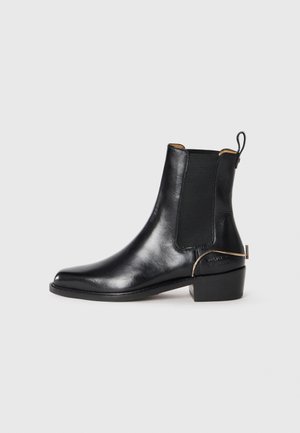 Bottine en cuir noir avec des panneaux latéraux élastiques, un petit talon carré et une touche dorée à l'arrière. Surface lisse, forme épurée.