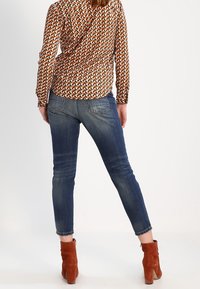 Mönstrad långärmad topp i brunt, orange och krämfärgat, i kombination med blå denim skinny jeans och klackade ankelskor i rostfärgad nyans.