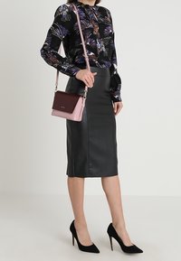 Svart blus med färgglatt blommönster, kombinerad med en figurnära skinnkjol. Accessoarer inkluderar en rosa axelväska och svarta klackskor.