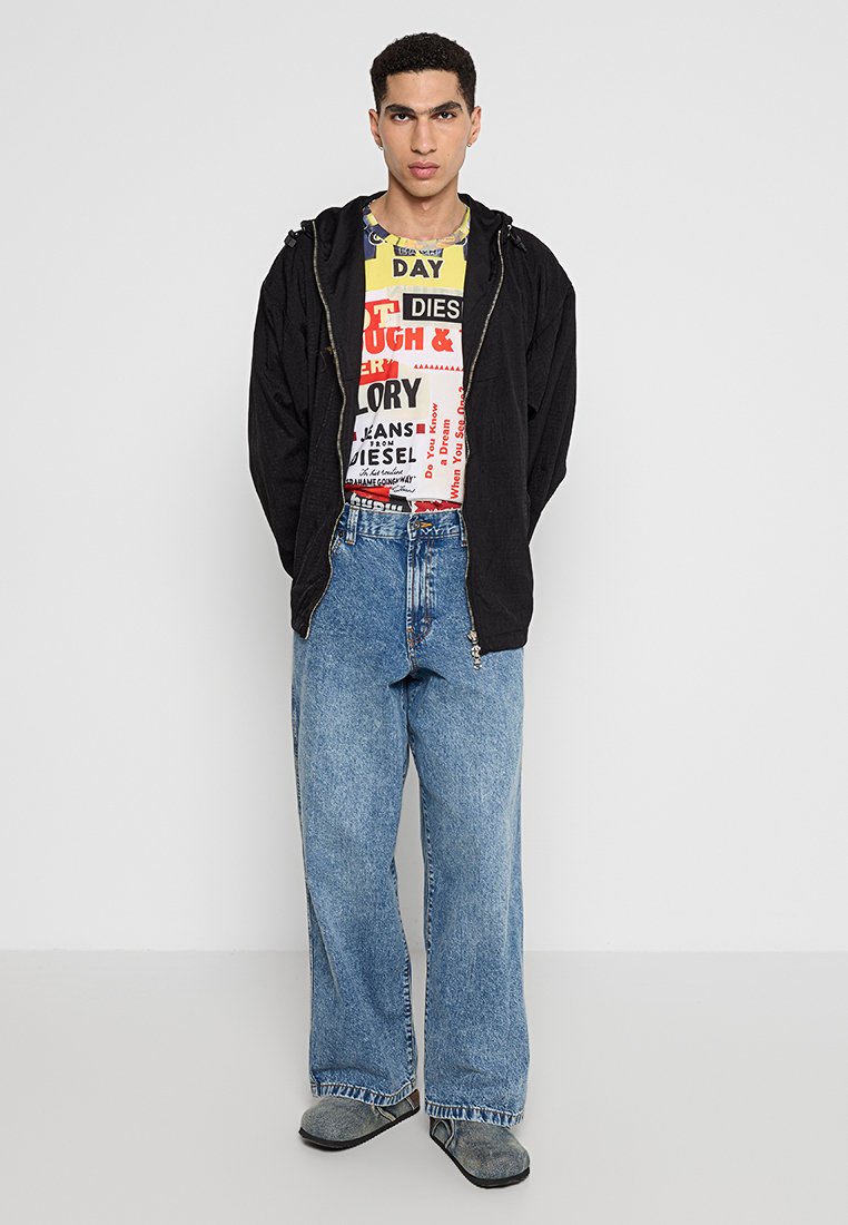 Schwarze Zip-Hoodie, grafisches gelb-rot T-Shirt, hochtaillierte blaue Jeans und graue Slipper. Schlichte Texturen und lässige Passform.