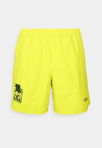 Bright yellow swim shorts with an elastic waistband, featuring a black graphic design on the left leg and a logo patch on the right hem.