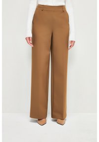 Pantalon à jambes larges en tissu marron chaud. Il présente un devant plat, deux poches latérales et des passants pour ceinture. Texture lisse avec une coupe structurée.