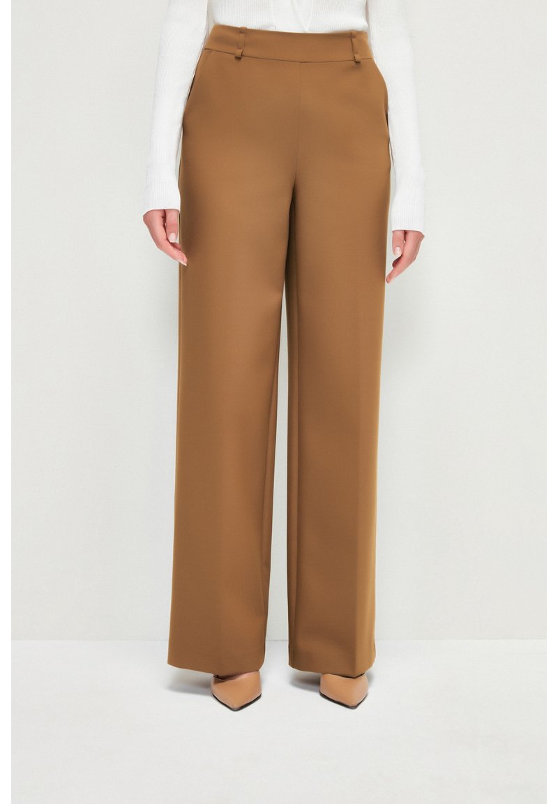 Pantalon à jambes larges en tissu marron chaud. Il présente un devant plat, deux poches latérales et des passants pour ceinture. Texture lisse avec une coupe structurée.