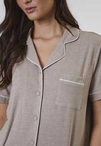 Hellbraunes, geripptes Hemd mit kurzen Ärmeln und Knöpfen, mit weißem Paspel am Kragen und an der Tasche, ausgestattet mit einer Brusttasche.