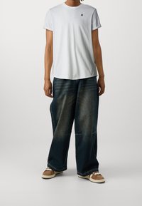 Vit bomull t-shirt med uppväljda ärmar, parat med lediga mörka denimjeans med ett urtvättat mönster. Bruna sneakers med vita inslag.