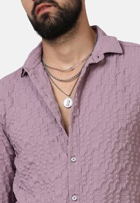 Camicia lavanda strutturata con colletto button-down, caratterizzata da un tessuto a fantasia, tre catene argentate e un collare con pendente prominente.