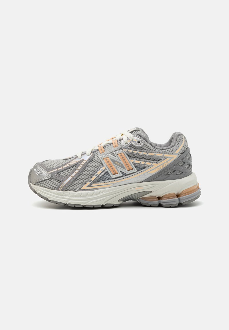 Chaussure de sport grise avec tige en mesh et accents synthétiques, présentant des détails orange, un bout arrondi et une semelle texturée et rembourrée.