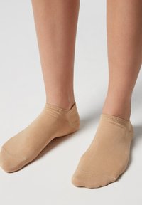Calcetines tobilleros beige con una textura lisa y acanalada, que presentan una puntera redondeada y un diseño de corte bajo, reposando sobre pies descalzos.