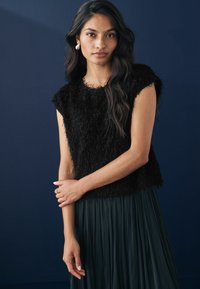 Must värviline lühikeste varrukatega särk, millel on tekstureeritud, karvane välimus, koos voolava, volditud tumeroheline seelik sinise tausta ees.