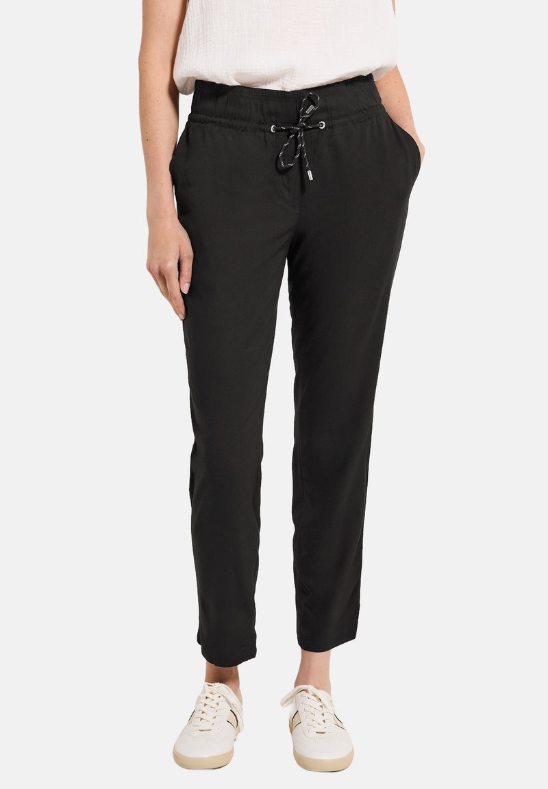 Zwarte, tapered broek met een elastische tailleband en trekkoord. Voorzien van zijzakken, een gladde textuur en een cropped lengte. G gedragen met witte sneakers.