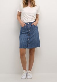 Jeanskjol med vertikala vita ränder, knälängd, med framknäppning och sidofickor, kombinerad med en vit t-shirt med V-ringning.