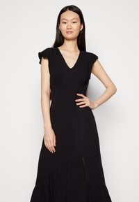 Vestido maxi preto com um decote em V profundo, mangas curtas com babados, cintura franzida e uma saia evasê com uma fenda lateral e textura subtil.