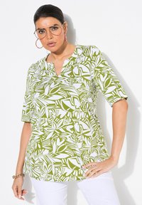 Top de color verde y blanco con estampado, de mangas cortas, escote en V y corte relajado. Presenta diseños abstractos de hojas sobre una tela ligera.