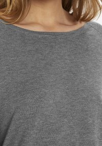 Top grigio a costine, con scollatura ampia e texture morbida, caratterizzato da una vestibilità rilassata e senza modelli o decorazioni visibili.