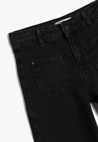 Jean en denim noir avec un design classique à cinq poches, un tissu texturé et une fermeture à bouton à la taille.