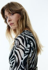 Schwarz-weiße Zebra-Print-Bluse mit Rüschenakzenten, aus transparenter Stoff gefertigt, mit Rundhalsausschnitt, langen Ärmeln und taillierter Silhouette.