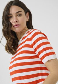 Top en tricot rayé avec de larges bandes rouges et blanches, manches courtes, encolure ronde et texture douce.
