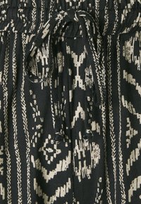 Zwarte stof met ingewikkelde witte patronen. Inclusief een trekkoord in de taille met gestructureerde accenten en verticale strepen in verschillende breedtes.