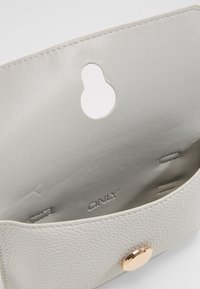 Szara skórzana kopertówka z teksturowanym wnętrzem, z złotym okrągłym zapięciem i wewnętrznym brandingiem. Otwarta konstrukcja z wycięciem w kształcie klucza.