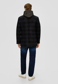Zwart en marineblauw geruit coat met een gewatteerde grijze capuchon, capuchon kraag, getailleerde pasvorm, gedragen over blauwe jeans en witte sneakers.