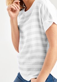 Hvidstribet t-shirt med subtile grå horisontale striber, rund halsudskæring og opsmøgte korte ærmer. Blødt tekstureret stof.