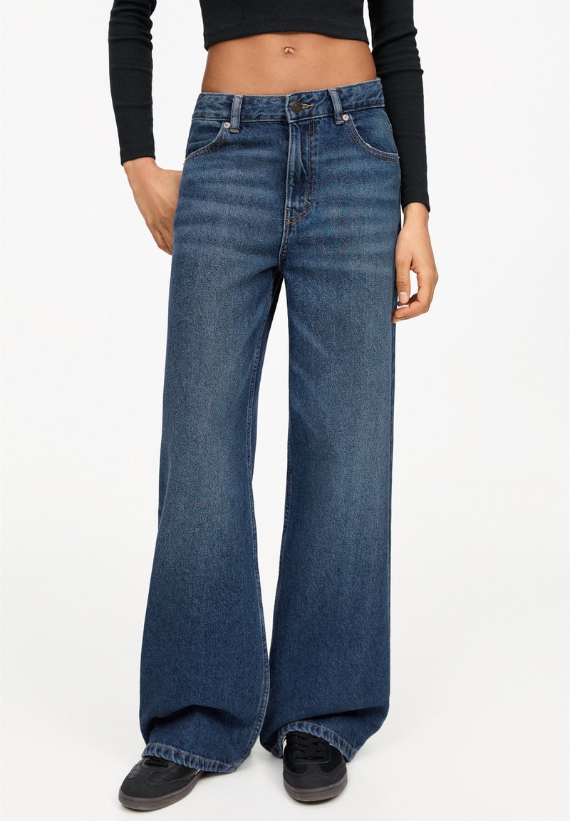 Vaqueros de pierna ancha de color azul oscuro con una cintura alta, que presentan un diseño clásico de cinco bolsillos y un desvanecimiento sutil. Fabricados en denim con una textura suave.